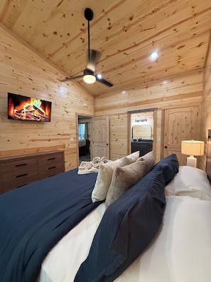 A wooden-paneled room with a bed, a television mounted on the wall, and a ceiling fan.