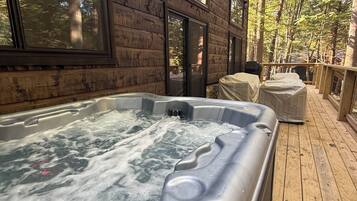 Une terrasse en bois avec un jacuzzi, de grandes fenêtres et une vue sur les arbres.