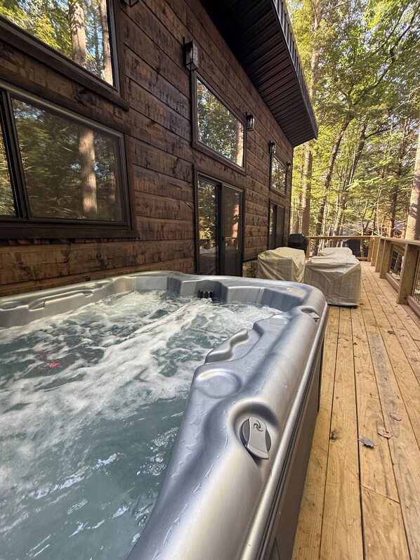 A wooden deck with a hot tub, large windows, and a view of trees.