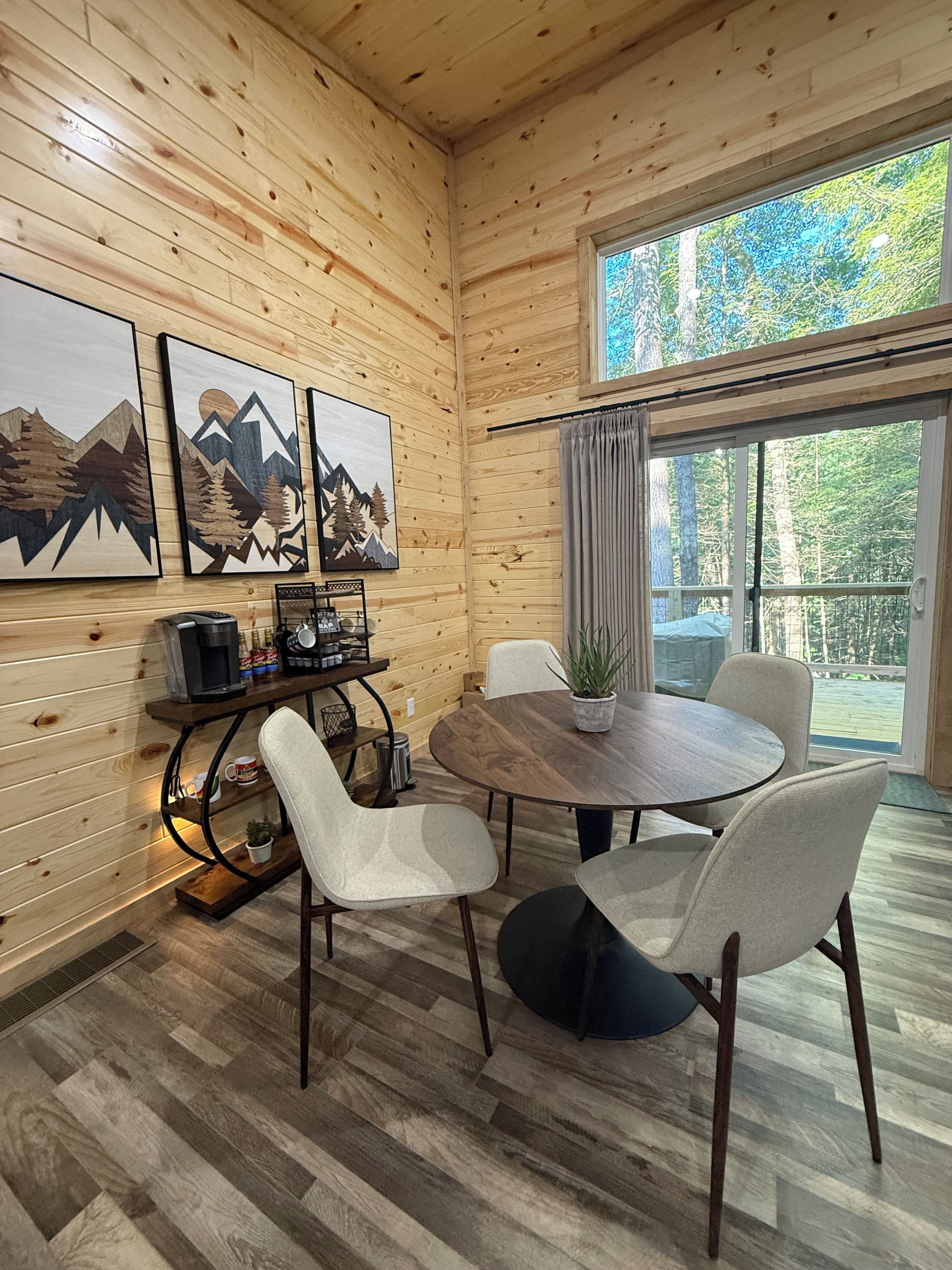 Un intérieur en bois comprenant une table à manger, des chaises, des œuvres d’art et une vue par la fenêtre.
