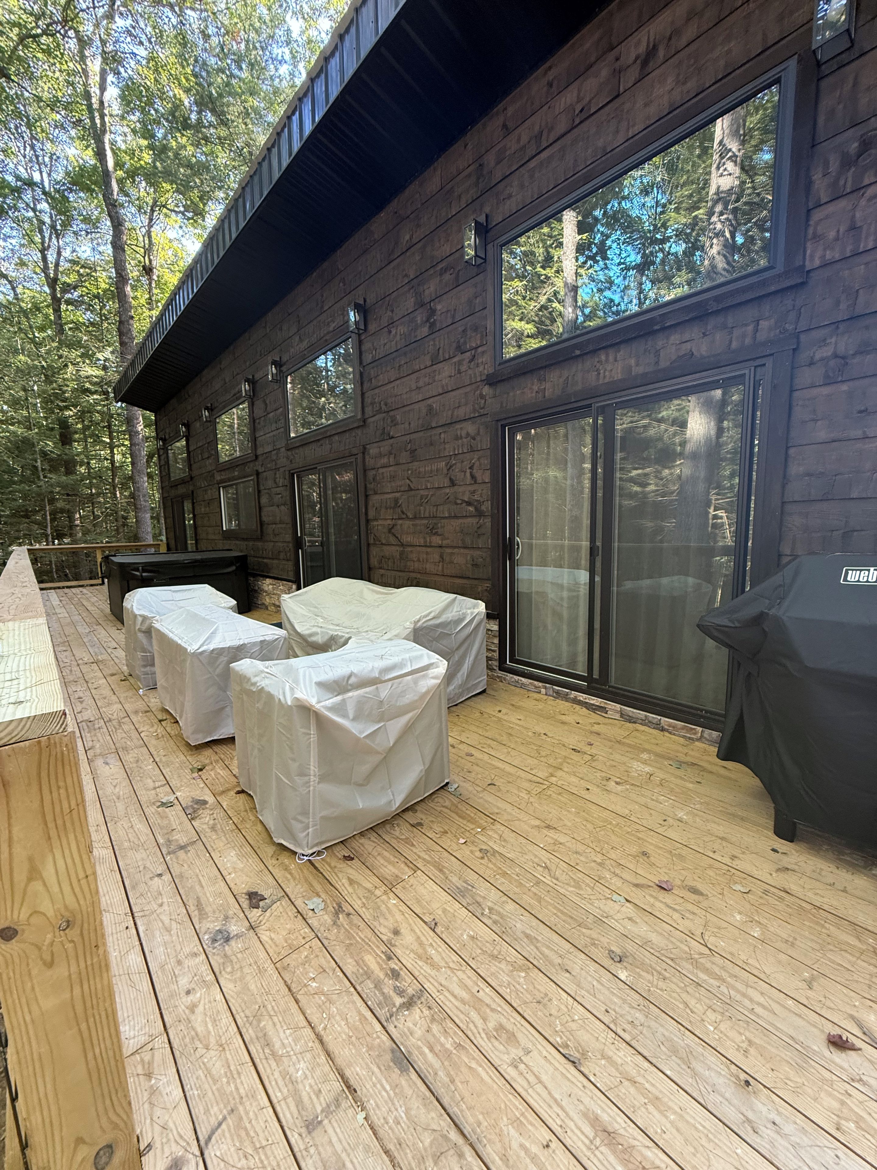 A wooden deck with covered seating and a grill, surrounded by a forest.