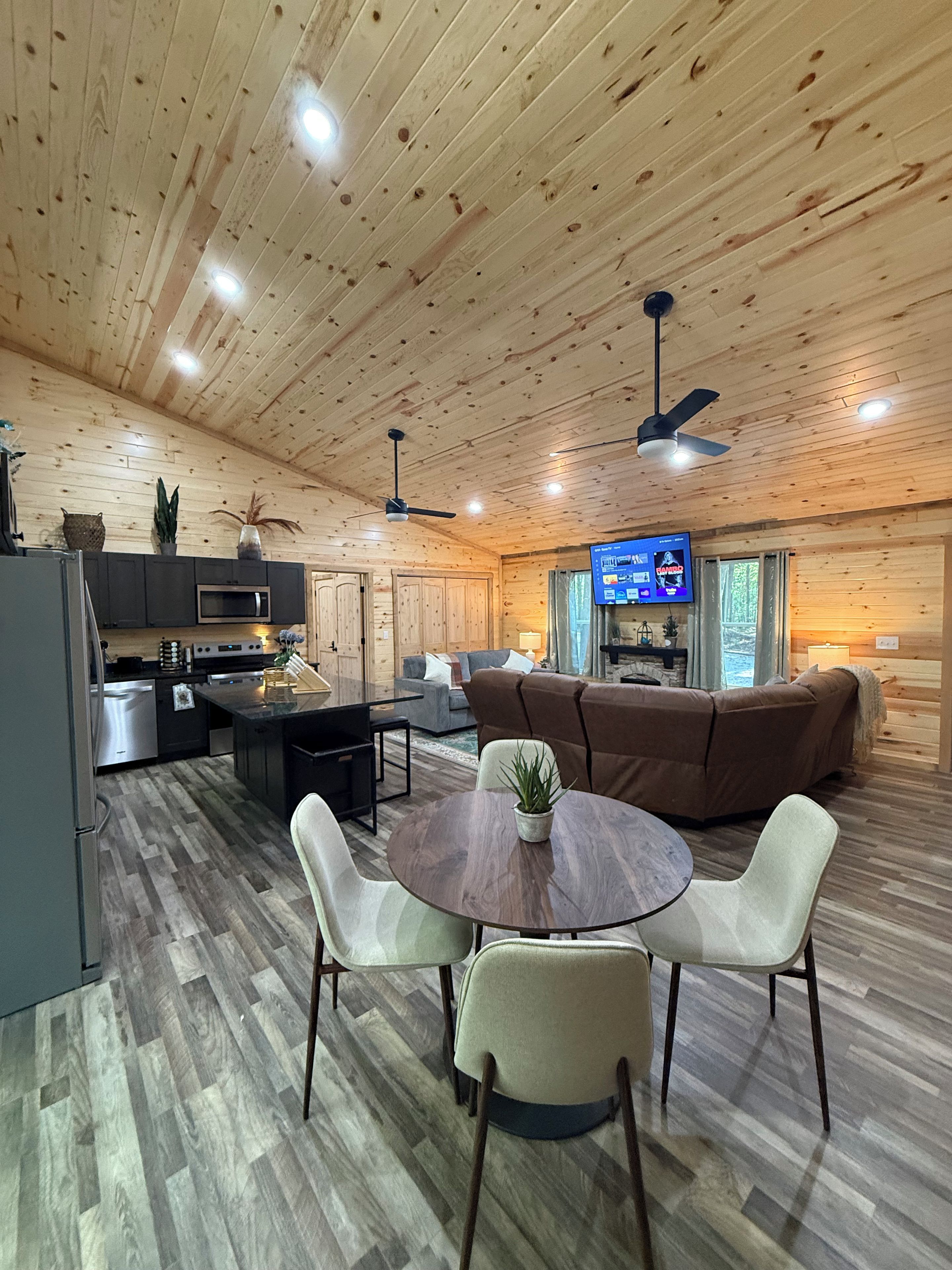 A spacious living area with a wooden ceiling, a dining table with chairs, a sofa, and a television.