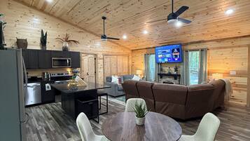 A spacious living area with a wooden ceiling, a dining table with chairs, a sofa, and a television.