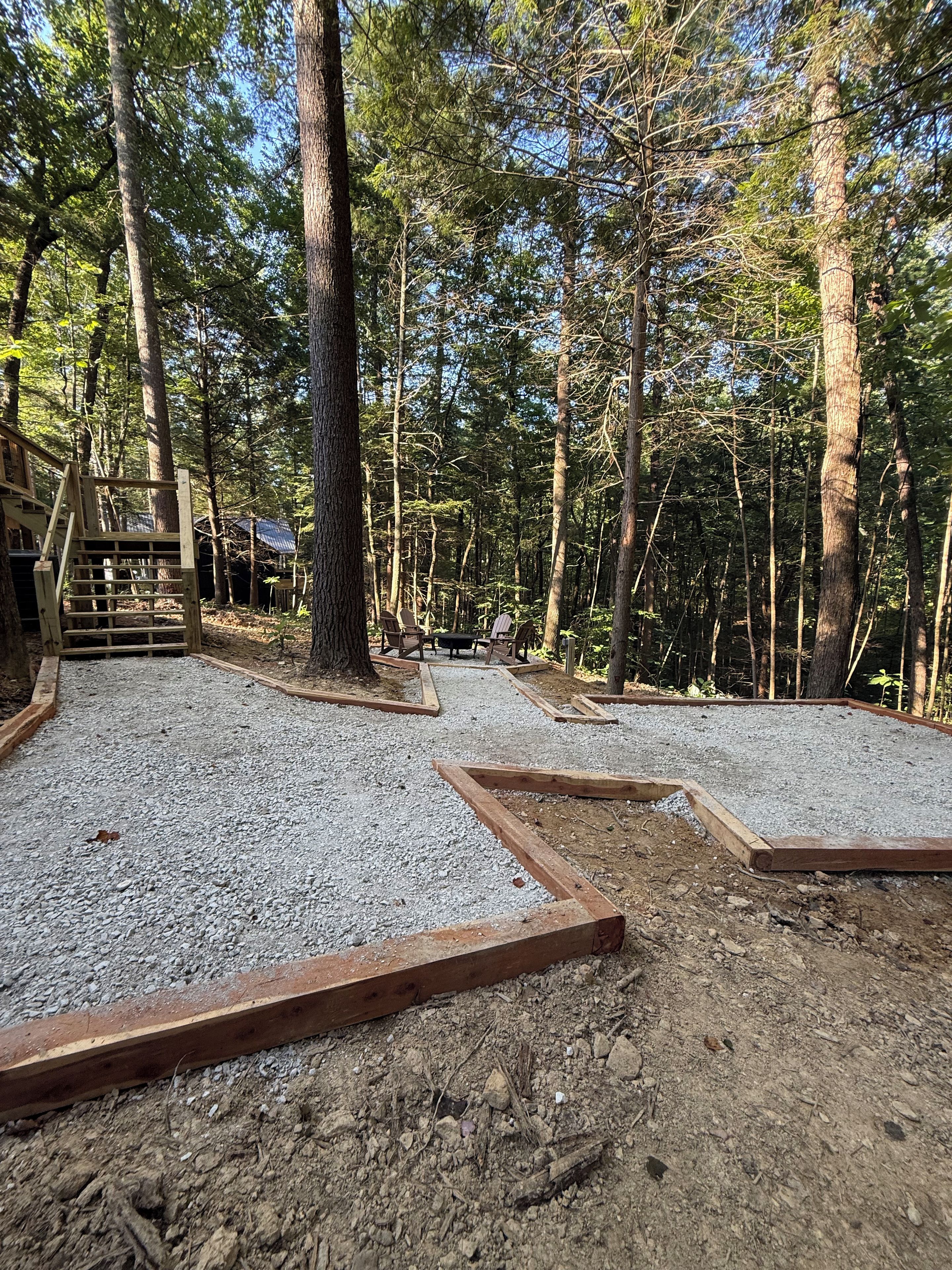 Une zone boisée avec un sentier de gravier, des structures en bois et un banc.
