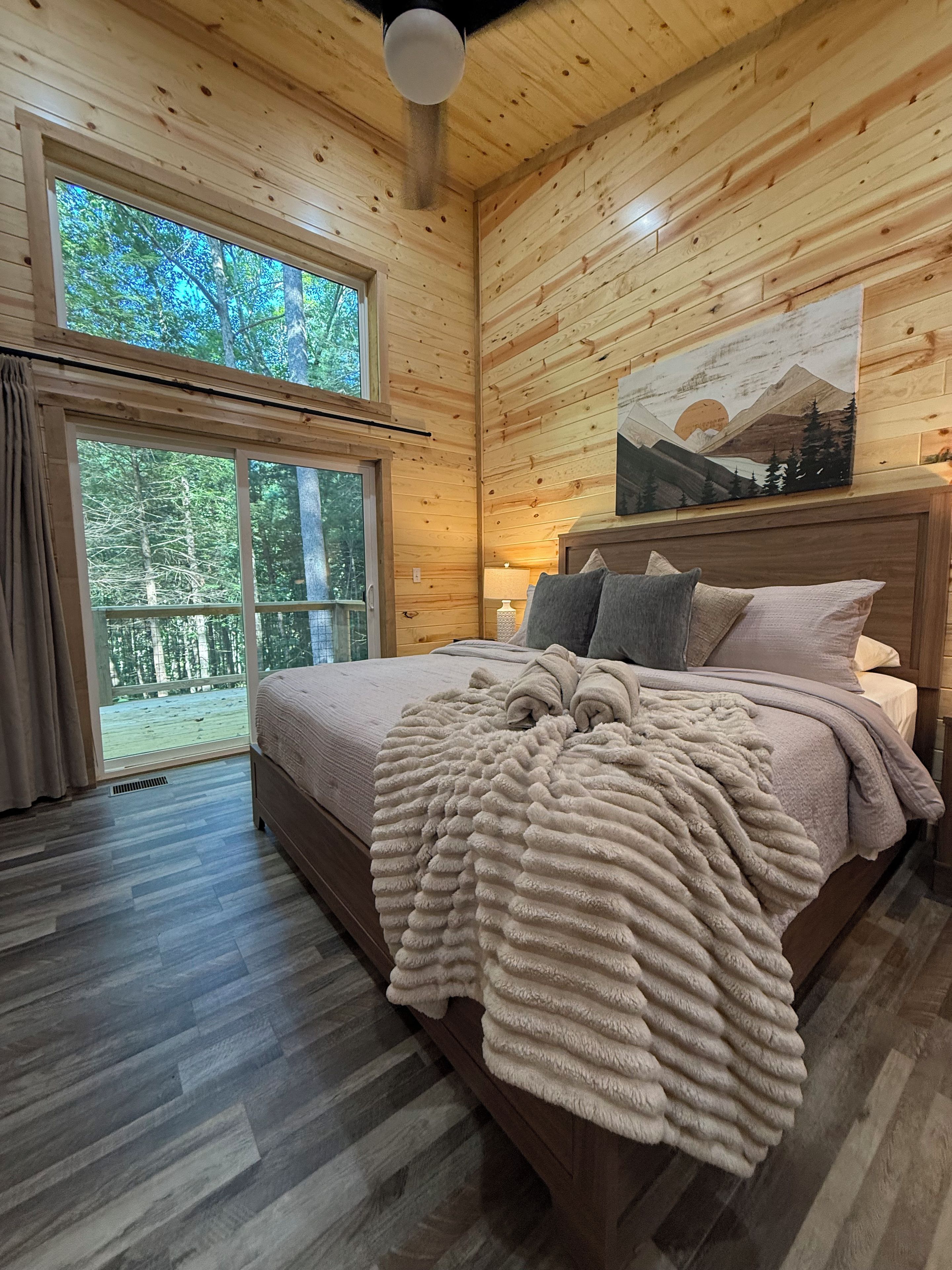 A wooden-paneled bedroom with a bed, a large window, and a painting on the wall.