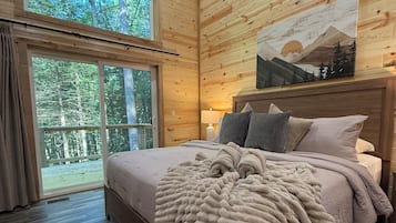 A wooden-paneled bedroom with a bed, a large window, and a painting on the wall.