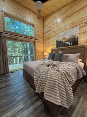 Ein Schlafzimmer mit Holzwänden, einem Bett, einem großen Fenster und einem Gemälde an der Wand.