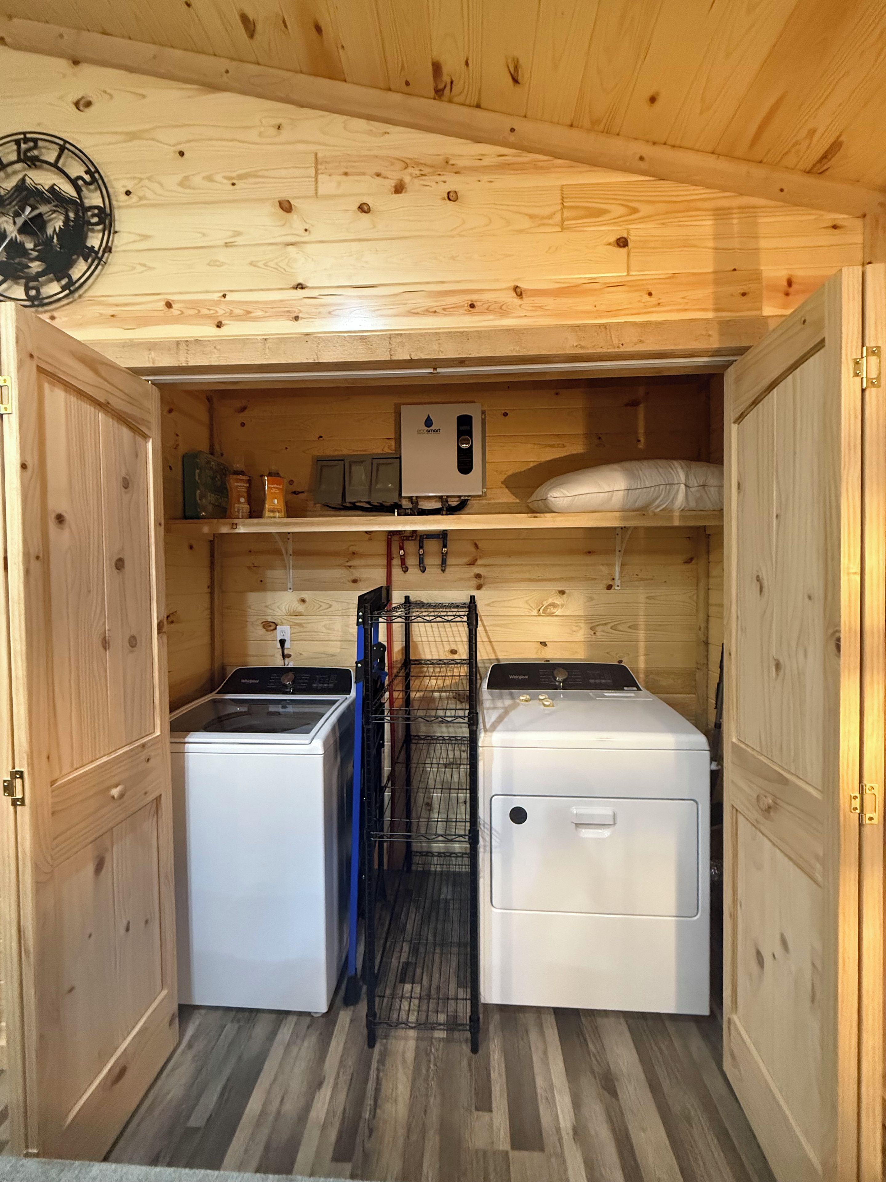 A compact laundry room with two washing machines, a drying rack, and a water heater.