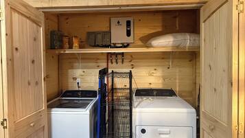 A compact laundry room with two washing machines, a drying rack, and a water heater.