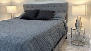 Camera da letto con un letto grande, due abat-jour, una testiera grigia imbottita e un quadro appeso al muro.
