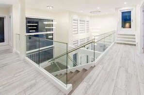 A modern interior with a glass railing staircase, white walls, and a wooden floor.