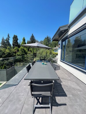 An outdoor patio with a grey table and chairs, a large umbrella, and a glass enclosure.