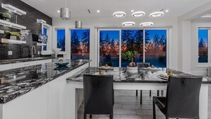 Una cucina moderna con una grande isola, sedie nere e vista sugli alberi attraverso ampie finestre.