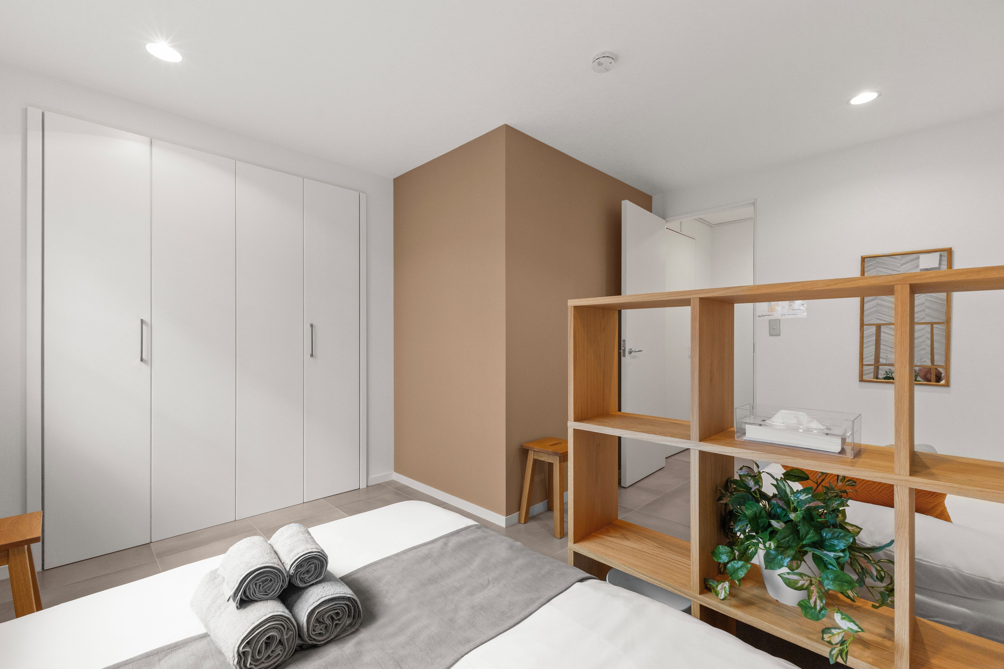 Quarto moderno com uma cama, uma estante de madeira, um banquinho e uma planta em vaso.