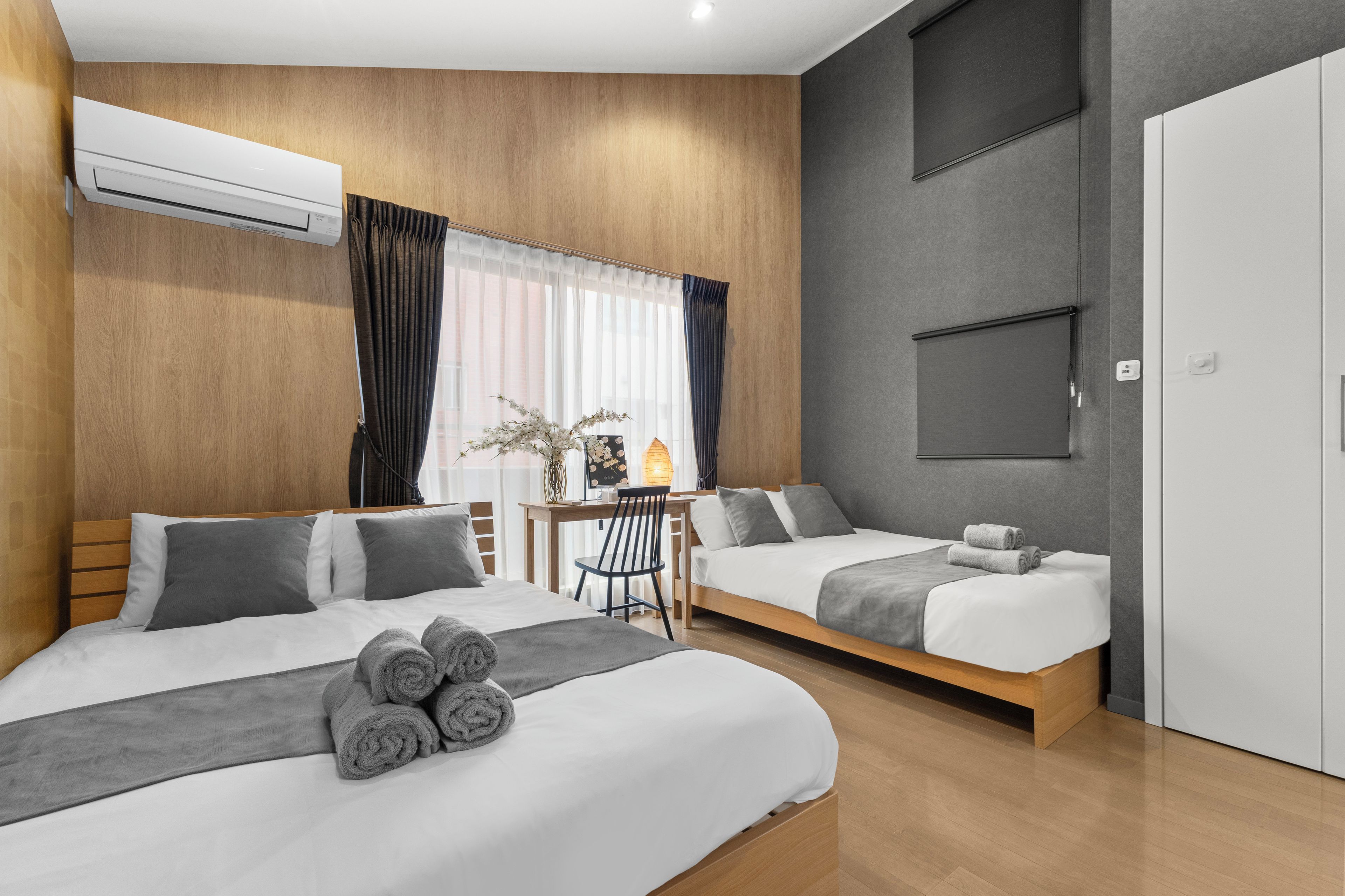 A hotel room with two beds, a desk, and an air conditioning unit.