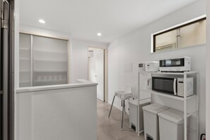 Ein modernes, minimalistisches Zimmer mit weißer Farbgestaltung, ausgestattet mit einer Mikrowelle, einem kleinen Kühlschrank und einem Sessel.