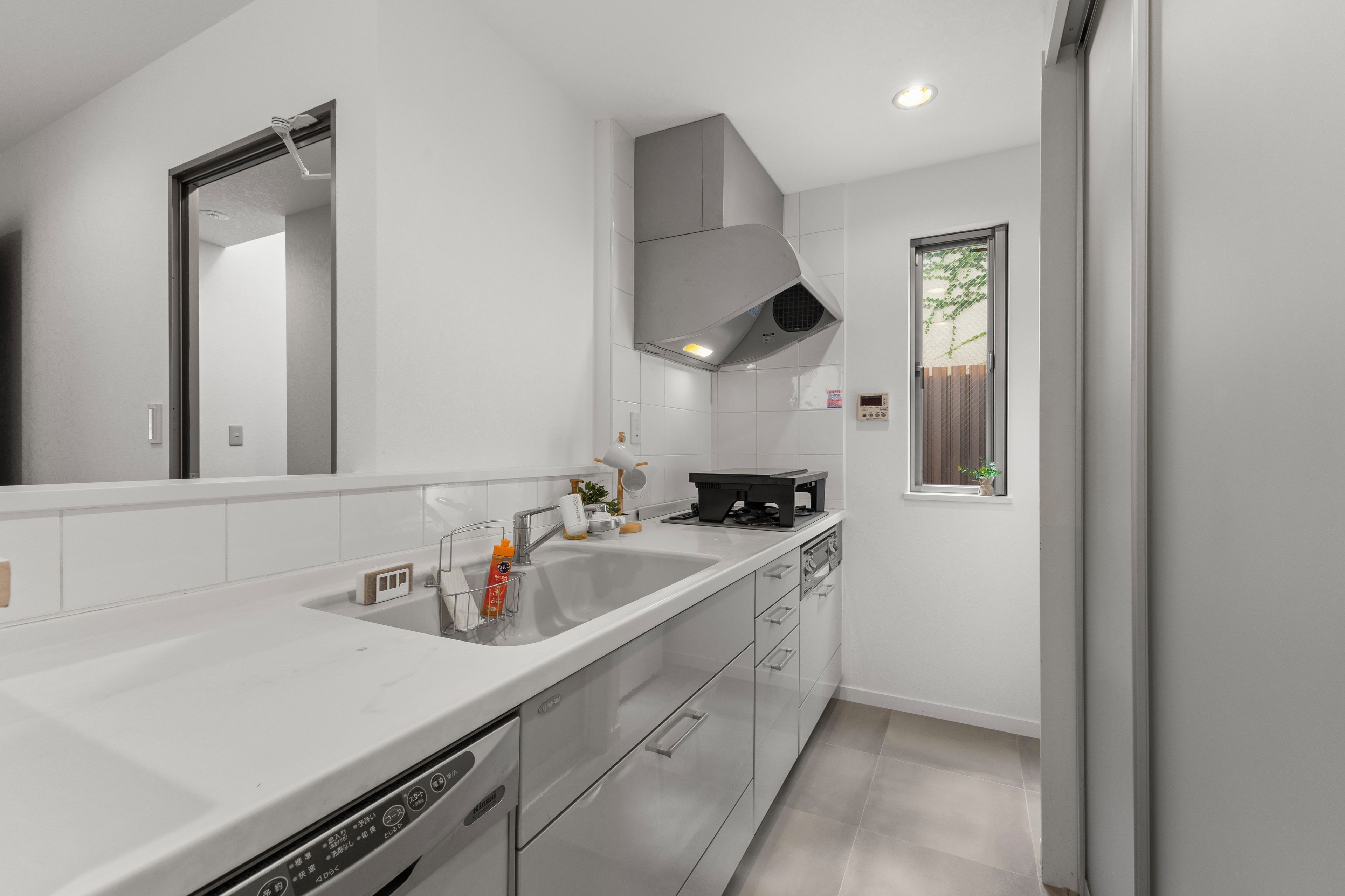 Une cuisine moderne avec un plan de travail blanc, des appareils en acier inoxydable et une fenêtre donnant sur un paysage verdoyant.