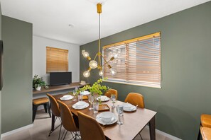 Ein Essbereich mit einem Tisch für vier Personen, Stühlen, einem Fernseher und einem Fenster mit Jalousien.