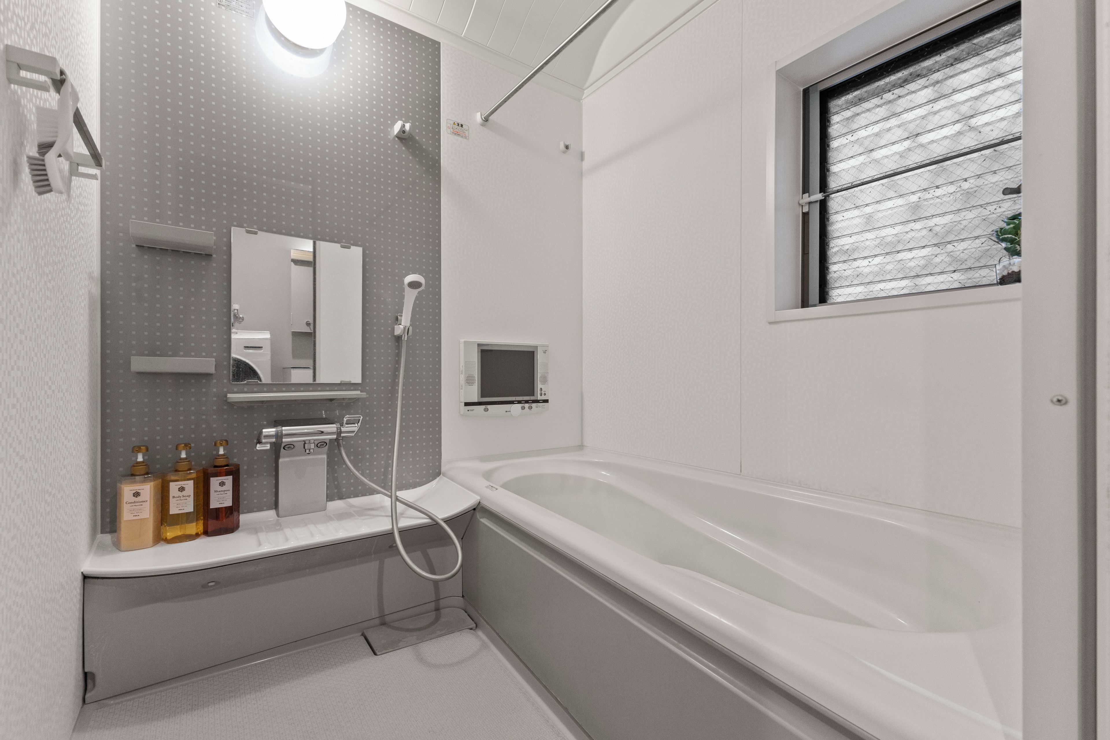 A modern bathroom with a bathtub, a shower, a toilet, and a sink. There are bottles of shampoo and conditioner on the counter.