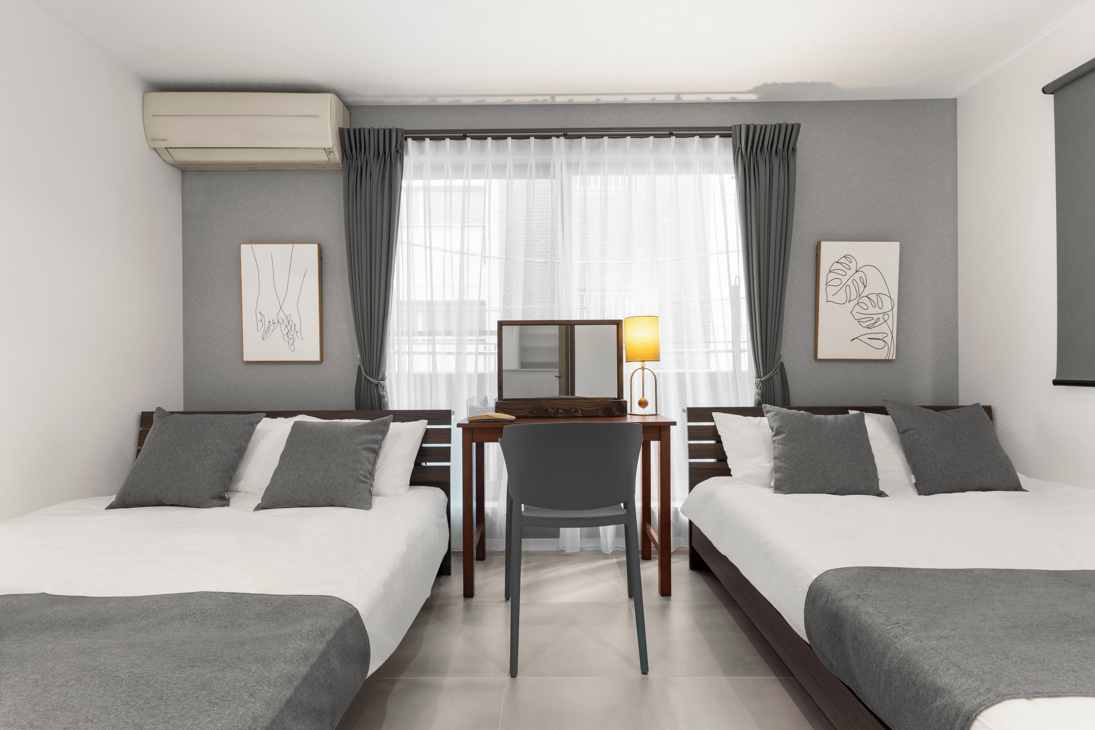 Une chambre d’hôtel avec deux lits, un bureau, une chaise, une lampe et des œuvres d’art accrochées aux murs.