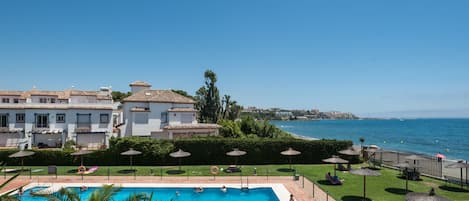 A swimming pool with a view of the sea, surrounded by umbrellas and a landscaped area.
