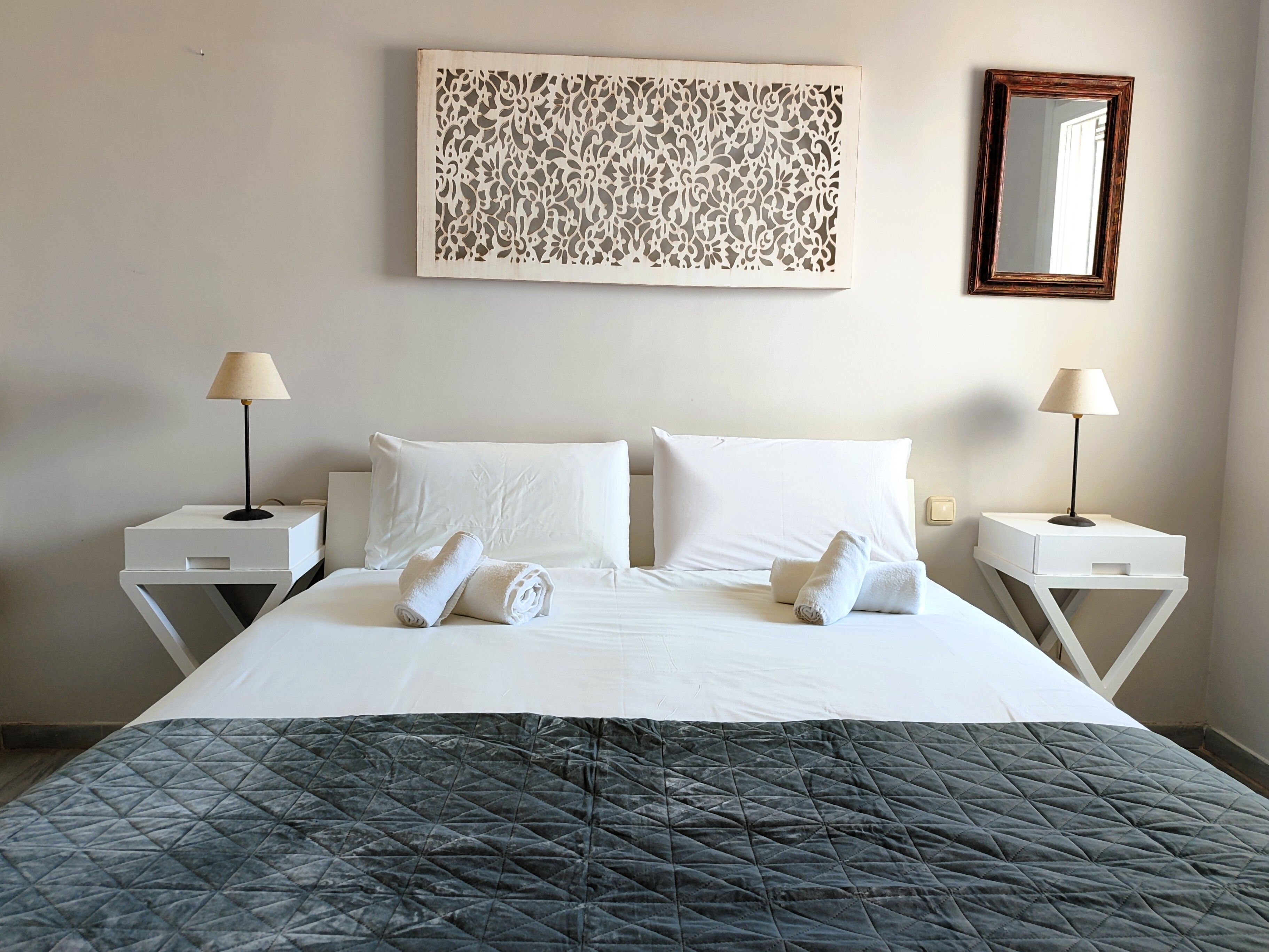 A hotel room with a bed, two bedside tables, a wall-mounted mirror, and a decorative panel.