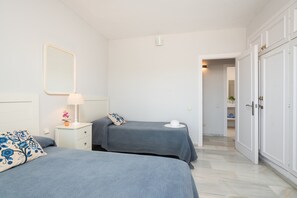 A bedroom with two beds, a bedside table with a lamp, and a mirror on the wall. - Selecta Estepona Sunrise (Estepona)