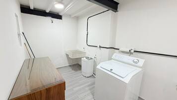 A compact laundry room with a washing machine, a small sink, and a trash bin.