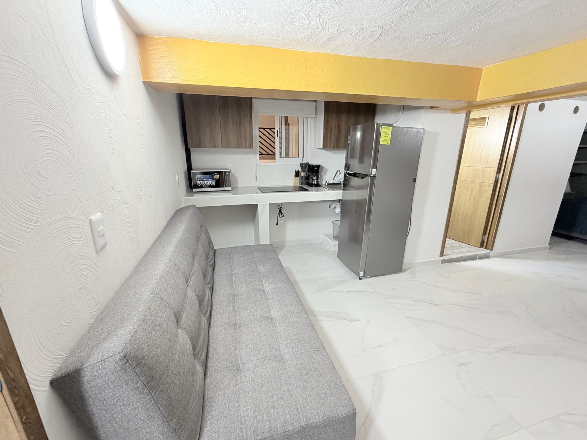 A compact living space with a kitchenette, a grey sofa, and a tiled floor.