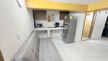 A compact living space with a kitchenette, a grey sofa, and a tiled floor.