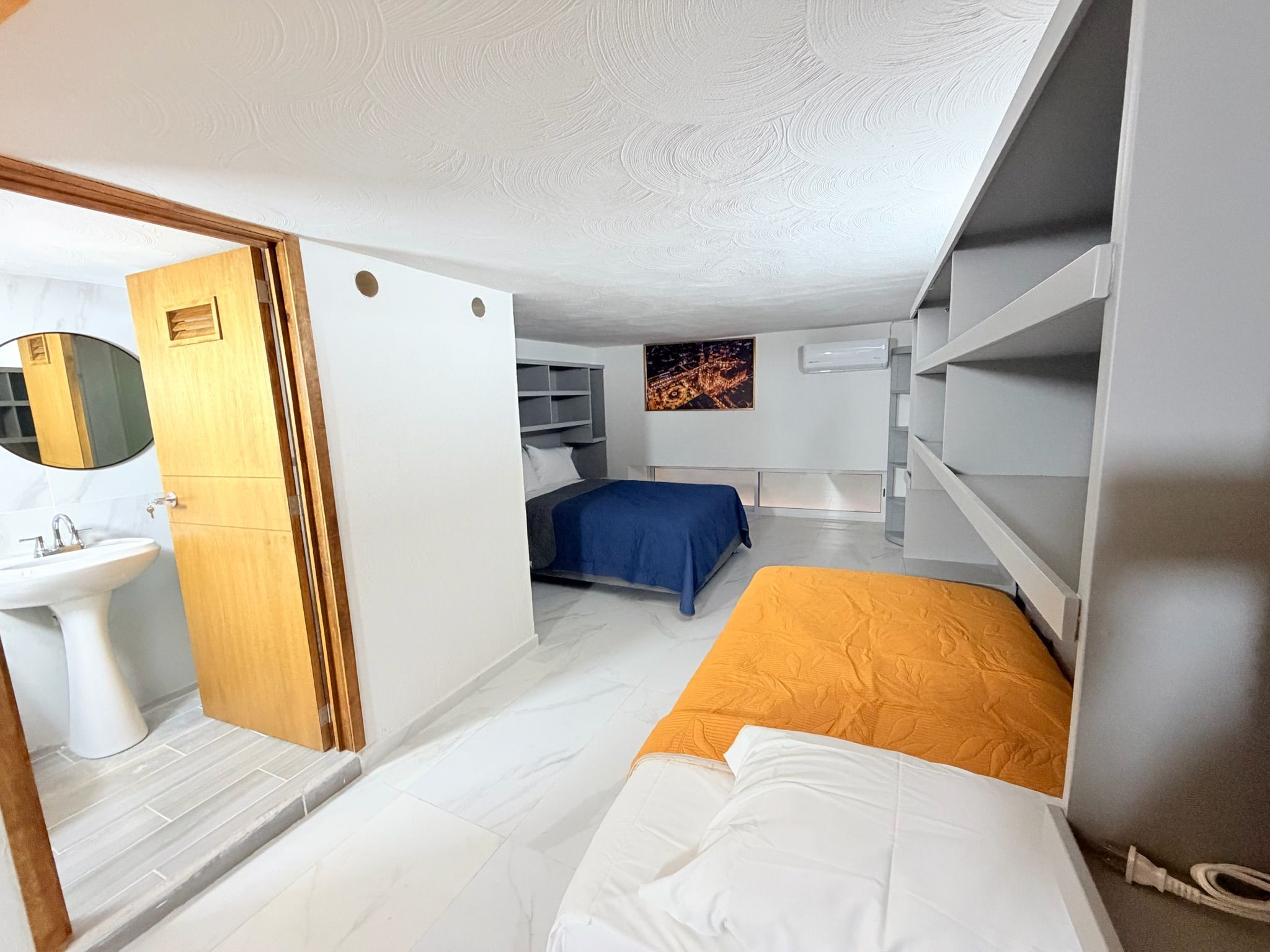 Een kleine hotelkamer met een bed, nachtkastje, spiegel, wastafel en een raam met uitzicht op de stad.