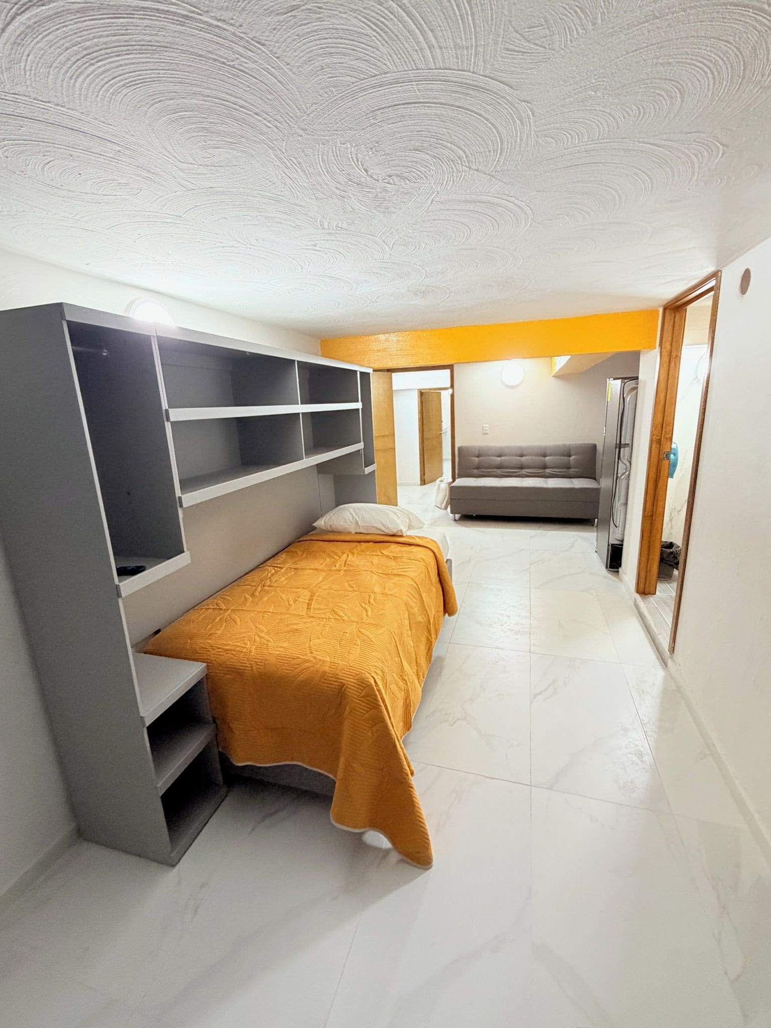A bedroom with a bed, a sofa, and a built-in shelf unit.