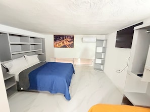A compact bedroom with a bed, built-in shelving, a flat-screen TV, and a wall-mounted air conditioner. - Cathedral Centro Histórico D9 (Guadalajara)