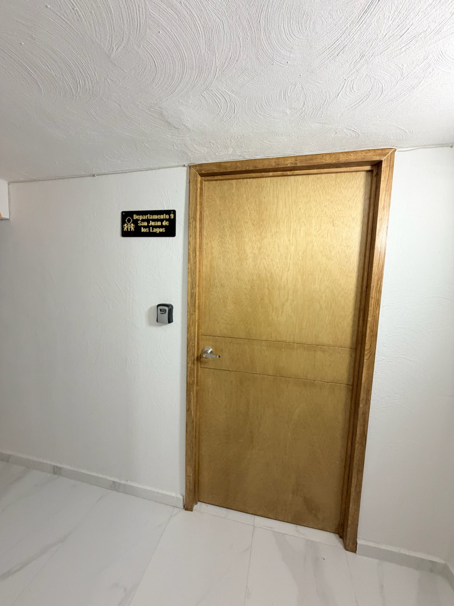 Una puerta de madera cerrada con un letrero encima que dice 'Departamento 9 San Juan de los Lagos'.