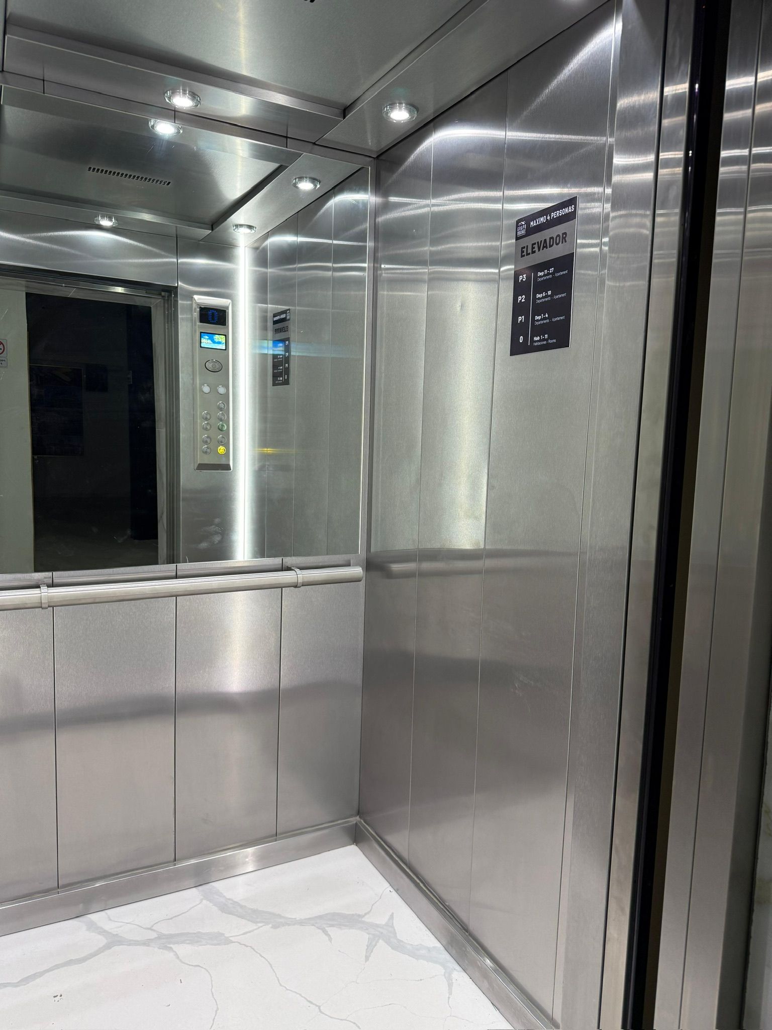 Interieur van een lift met metalen wanden, een digitaal display en een bord met de maximale capaciteit en verdiepingen.
