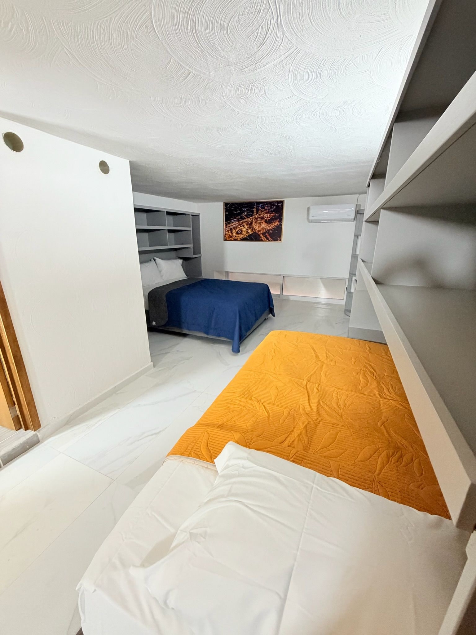A compact bedroom with a bed, a blue bedspread, and a wall-mounted shelf.