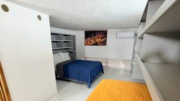 A compact bedroom with a bed, a blue bedspread, and a wall-mounted shelf.