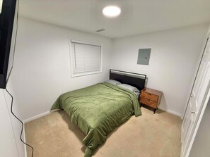 Quarto com uma cama de solteiro, mesa de cabeceira, luminária na parede e janela com persianas.
