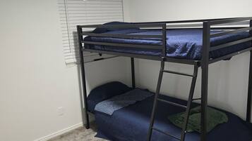 Een stapelbed met een ladder, een raam met zonwering en een vloerbedekking.