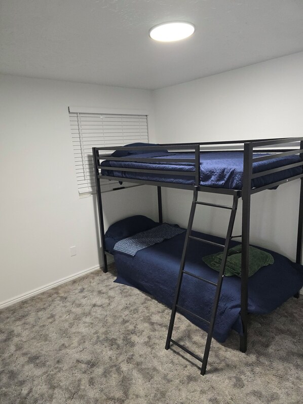 A bunk bed with a ladder, a window with blinds, and a carpeted floor.