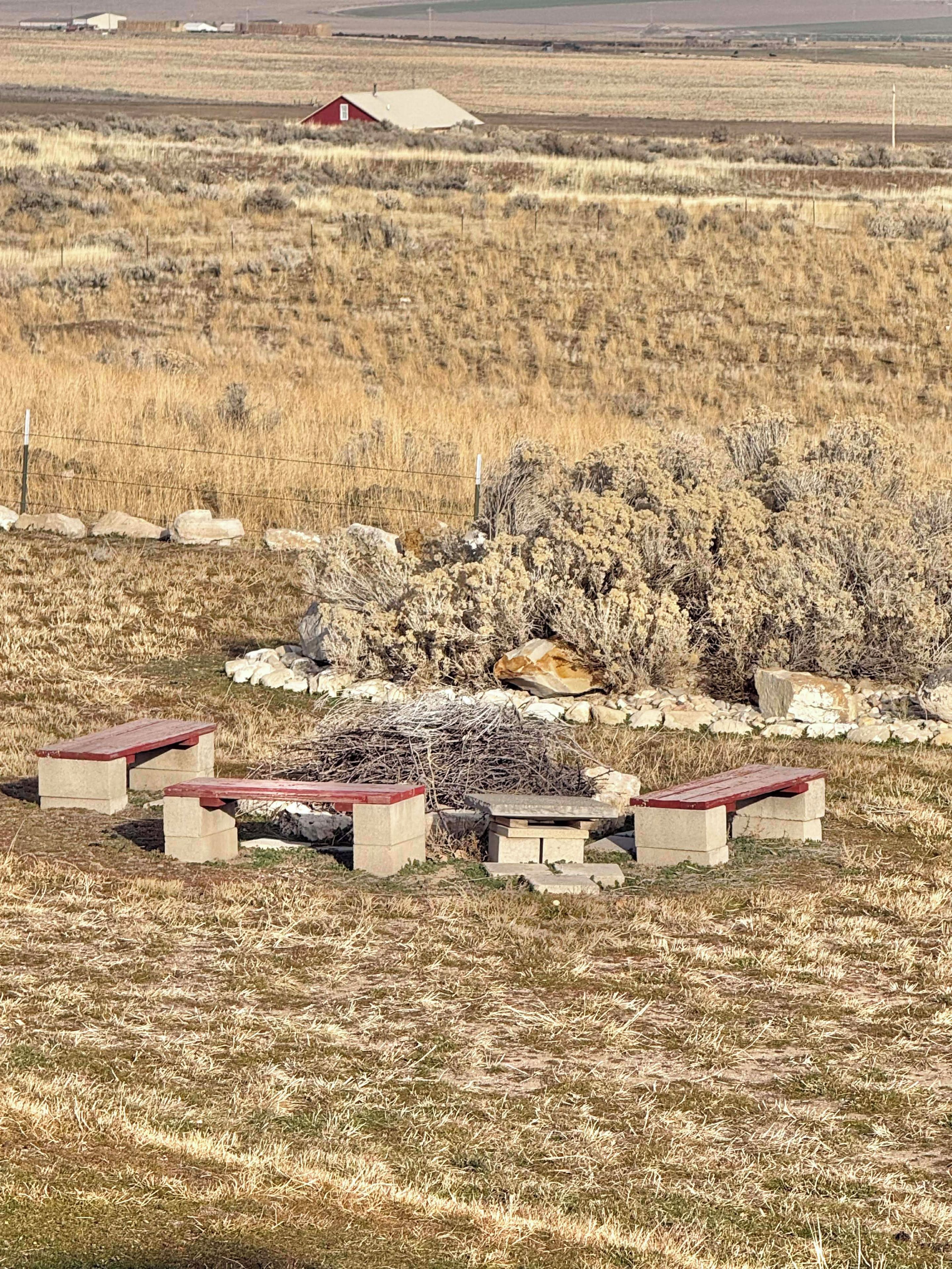 Un paisaje rural con un granero rojo, un muro de piedra y un grupo de mesas de picnic.