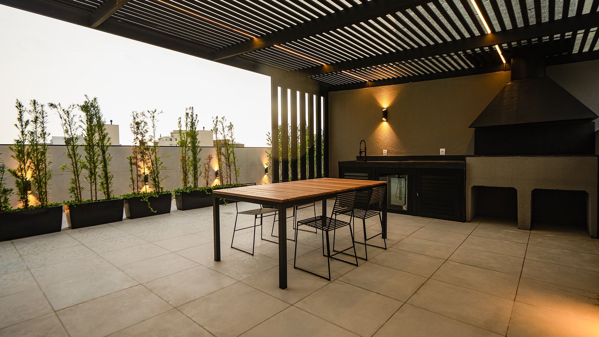 Um terraço no último andar com mesa e cadeiras, churrasqueira e jardins verticais.