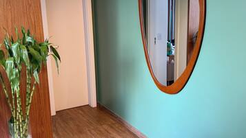 Um corredor com piso de madeira, parede verde e espelho com moldura de madeira.