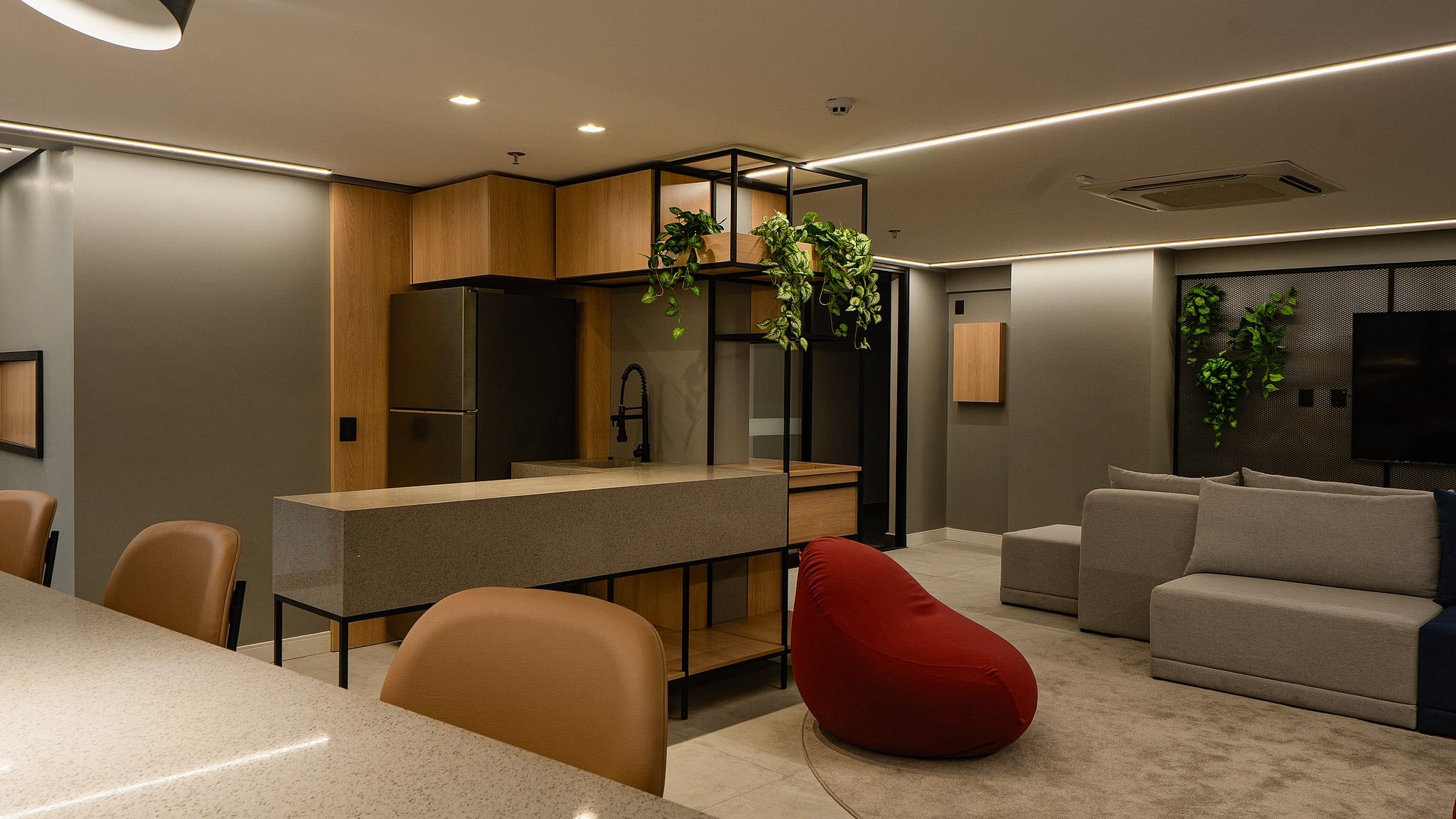 Uma sala de estar moderna com área de jantar, uma poltrona de couro vermelho e uma TV fixada na parede.