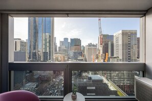 A room with a large window overlooking a cityscape with high-rise buildings and construction cranes. - Melbourne Skyline Views Modern 1BR with Pool & Gym (Melbourne)