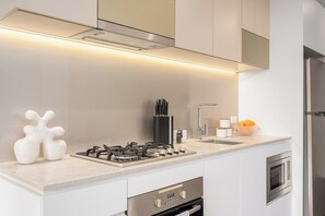 A modern kitchen with a gas stove, stainless steel appliances, and a microwave. - Melbourne Skyline Views Modern 1BR with Pool & Gym (Melbourne)