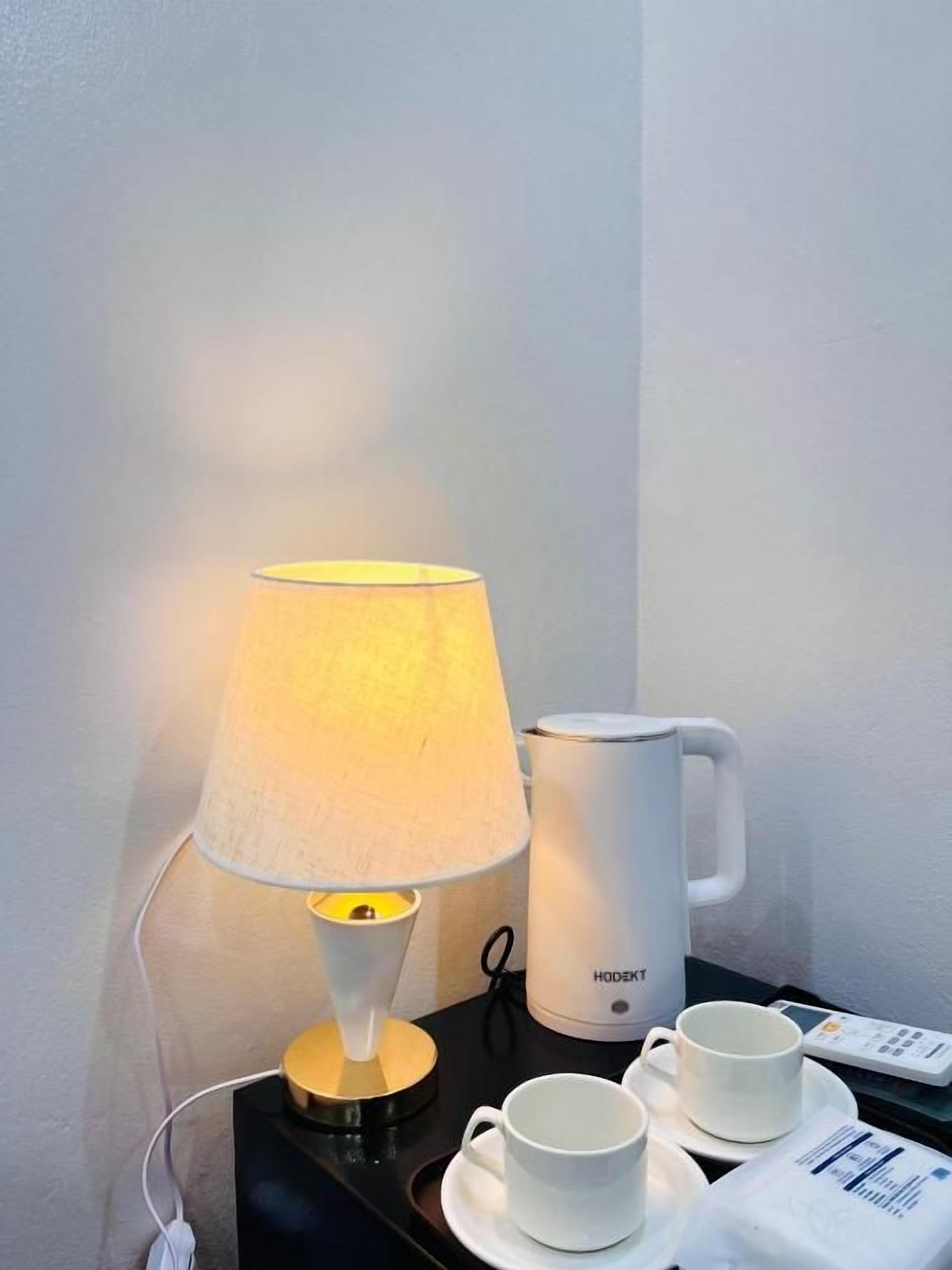 A bedside table with a lamp, a white mug, and a remote control.
