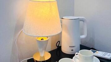 A bedside table with a lamp, a white mug, and a remote control.