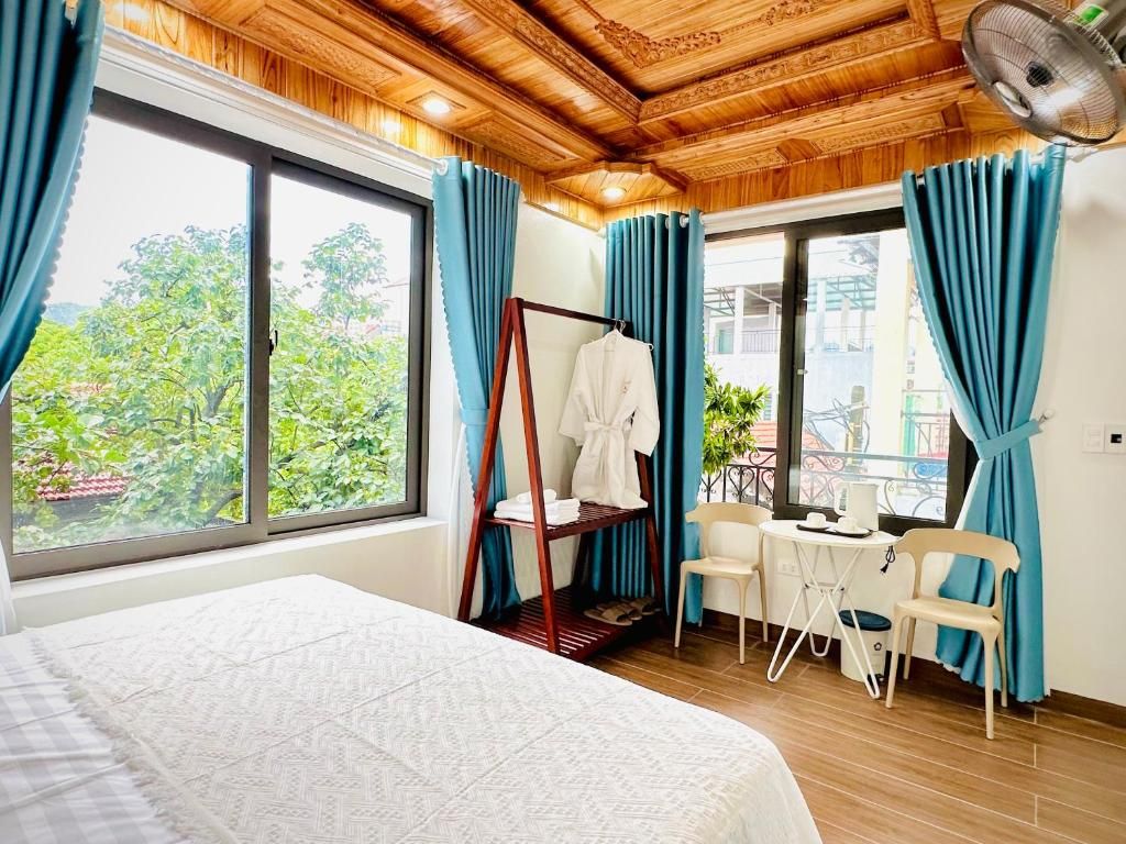 Habitación de hotel con cama, techo de madera, ventana con cortinas, mesa con sillas y vistas al balcón.