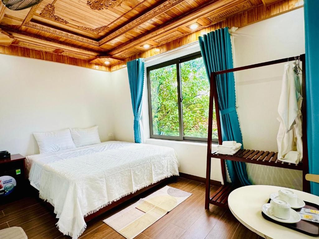 A bedroom with a wooden ceiling, a bed with a white bedspread, a window with curtains, a bunk bed, and a small table with cups.